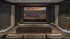 A photo of a home theater with a screensaver populated on the widescreen. There are two rows of chairs visible.